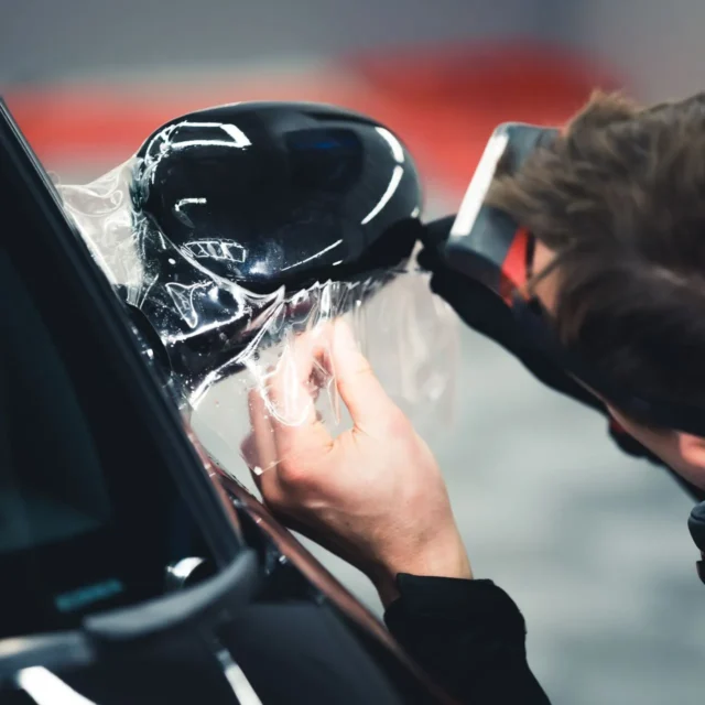 Installer fitting clear paint protection film over a black painted exterior mirror cap.