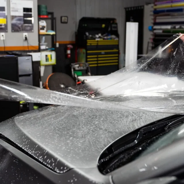 Installers stretching clear paint protection film over a silver car panel.